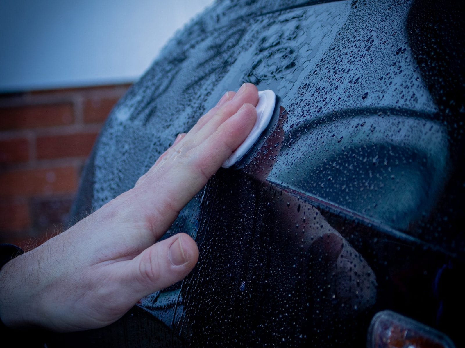 close up hand wiping wet car with cotton pad