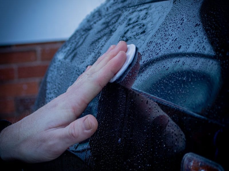 close up hand wiping wet car with cotton pad